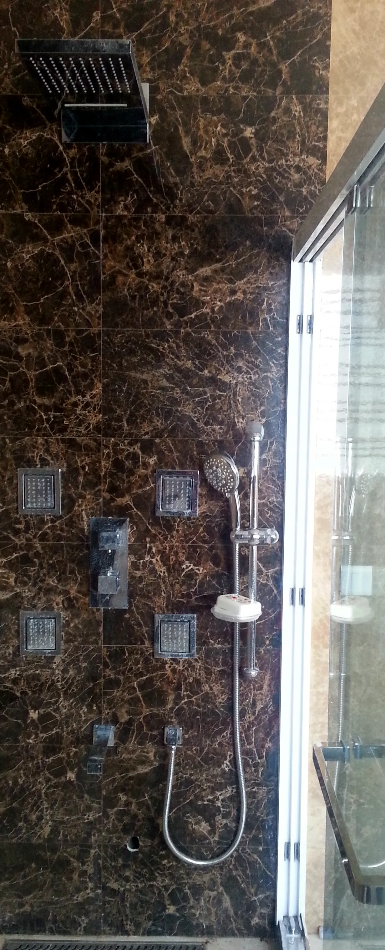 Finished shower on dark marble with a rain shower, four body jets, a concealed mixer, a hand shower on a slide rail and a spout