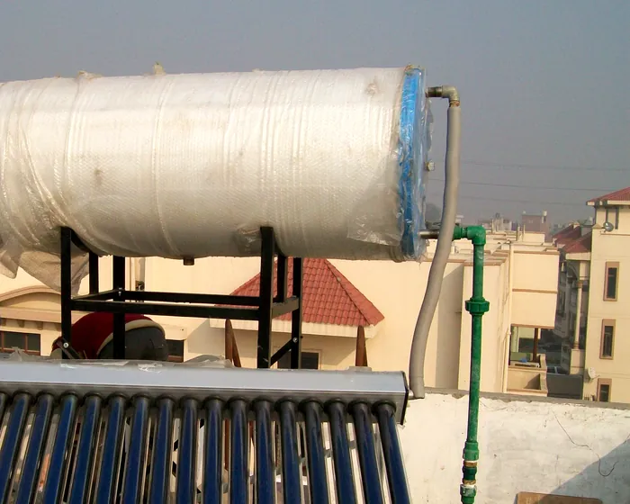 Solar water heater tank on a rooftop during installation, with the hot-water line coming off the tank and green PPR piping running down to the roof