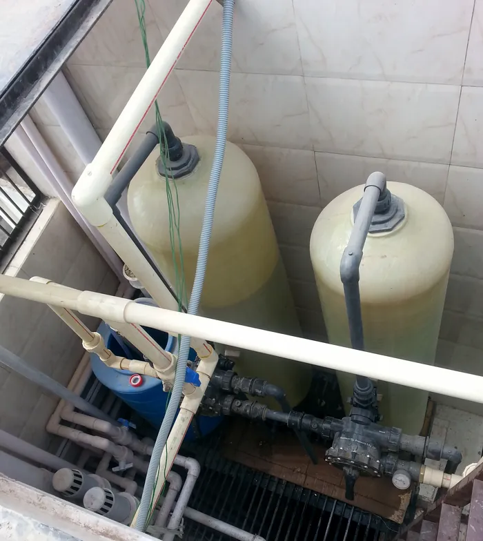 Top view of a water treatment set-up in a service shaft: two fibreglass vessels with multiport valves, a pressure gauge, a brine tank and CPVC and UPVC piping